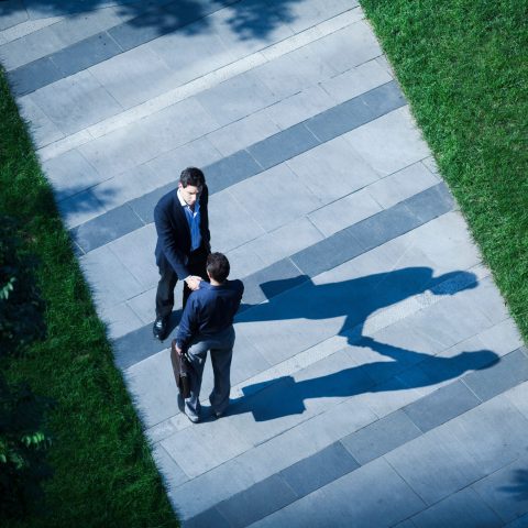Aerial view of two businessmen shaking hands on the sidewalk